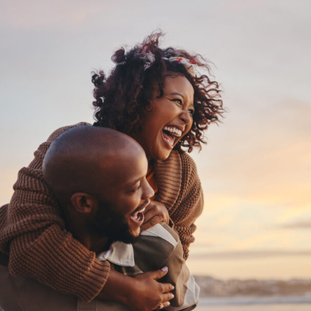 Black couple, travel and beach fun while laughing on sunset nature adventure and summer vacation or honeymoon with a piggy back ride. Comic, energy and black man and woman love on ocean holiday.